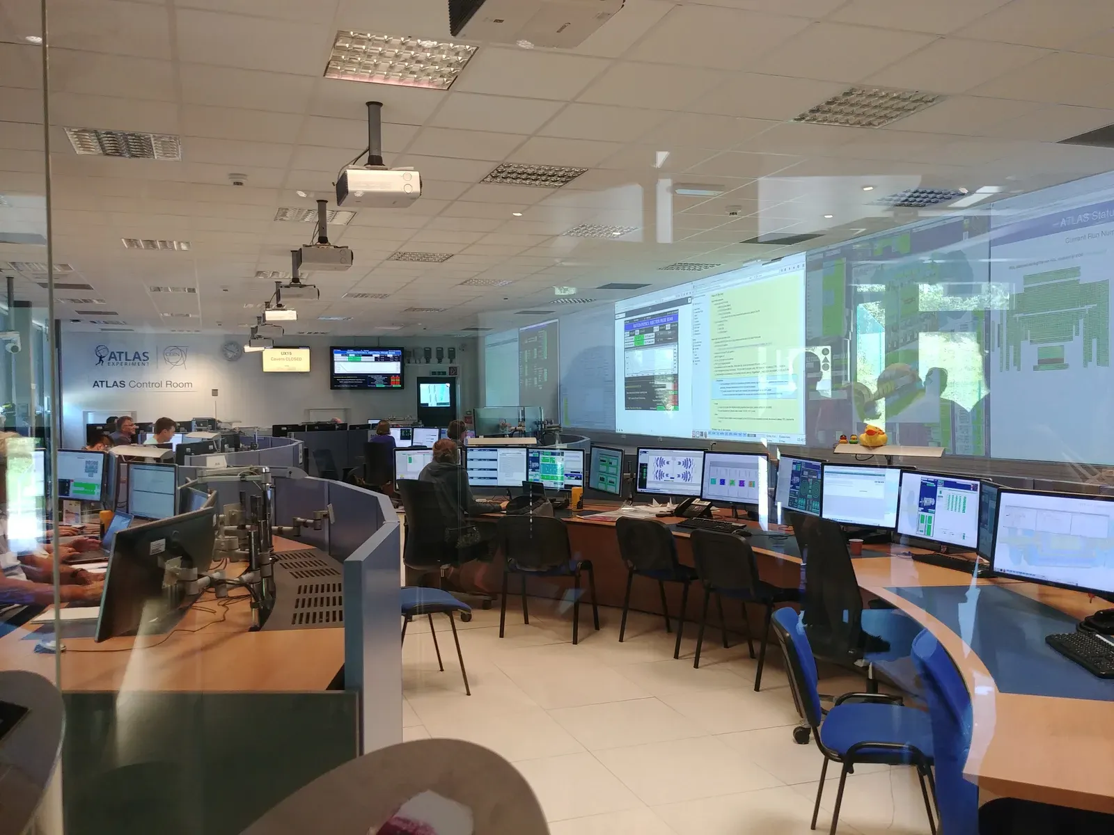 The ATLAS Control Room — banks of monitors and a large screen of run data, seen through glass.
